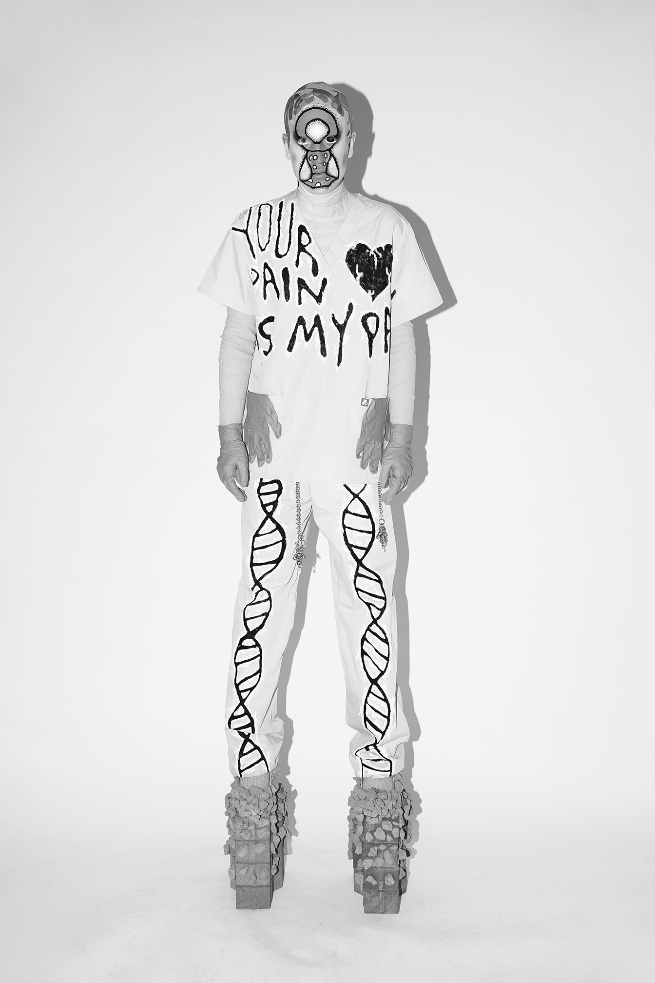 Jesse standing while looking at the camera with graphic facepaint on wearing scrubs against a white background